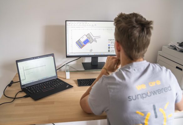 Mann sitzt vor einem Bildschrim und einem Laptop