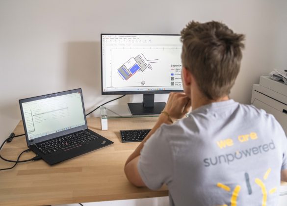 Mann sitzt vor einem Bildschrim und einem Laptop