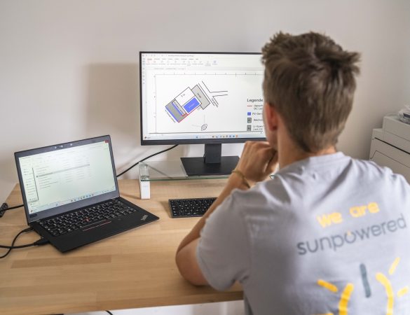 Mann sitzt vor einem Bildschrim und einem Laptop